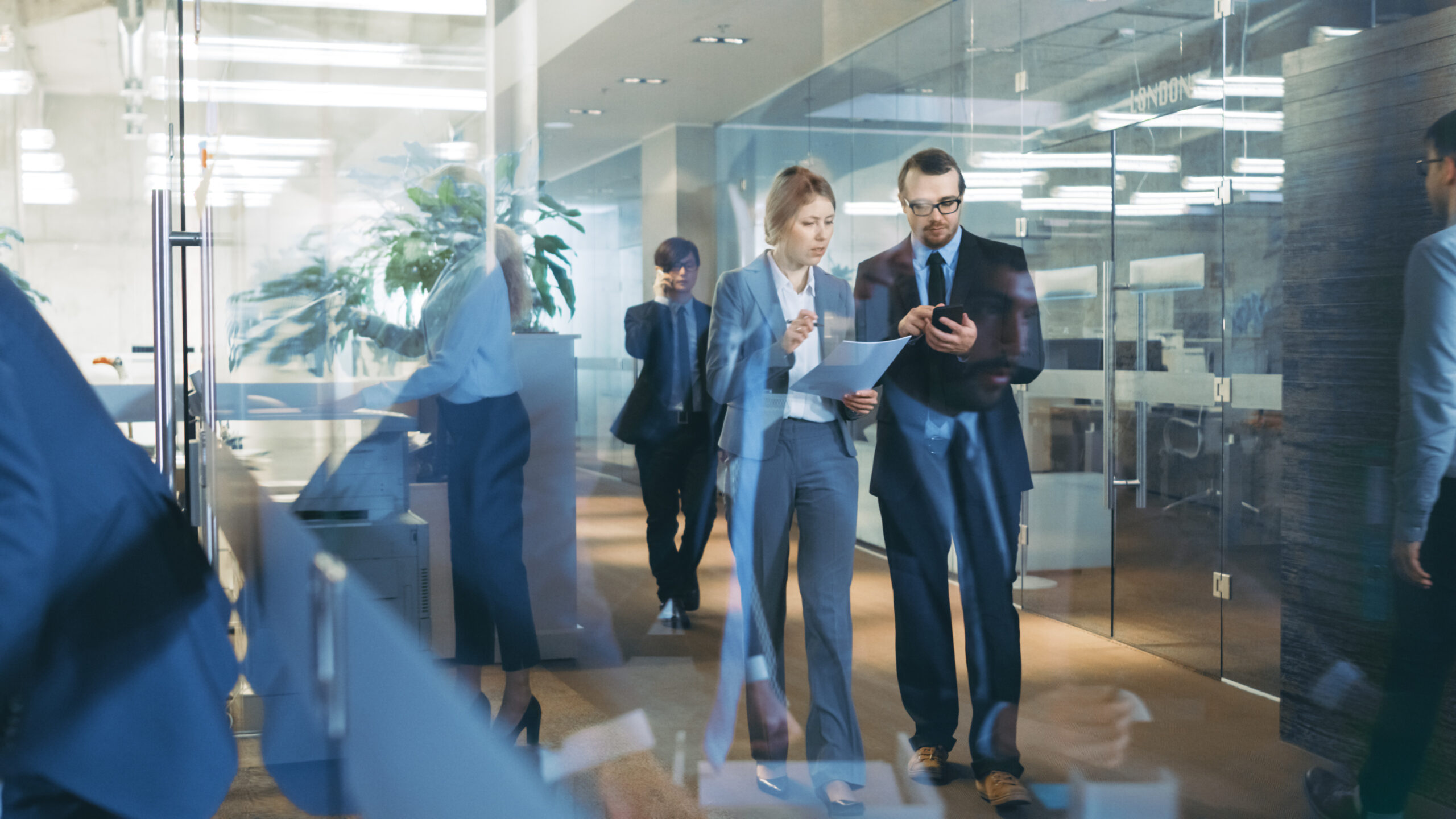 Business People Walking And Talking In The Hallway And Use Tablet Computer, Businessmen Have Conversation In The Office. Corporate Office With Many Busy Workers.